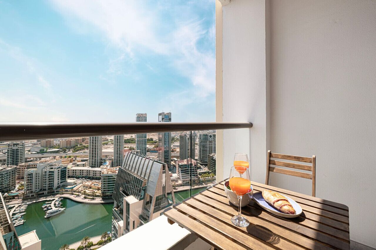 Un balcon avec une table dressée pour deux personnes, offrant une vue sur un port de plaisance et le paysage urbain.