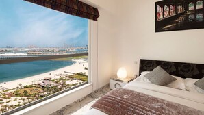 Een slaapkamer met een groot raam dat uitzicht biedt op een strand en stadsgezicht.