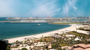 Een kustresort met een strand, jachthaven en moderne gebouwen op de achtergrond.