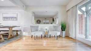 Ein geräumiges Wohnzimmer mit Holzboden, zwei grauen Polsterstühlen, einem kleinen Tisch, einem großen Spiegel und einer Topfpflanze.