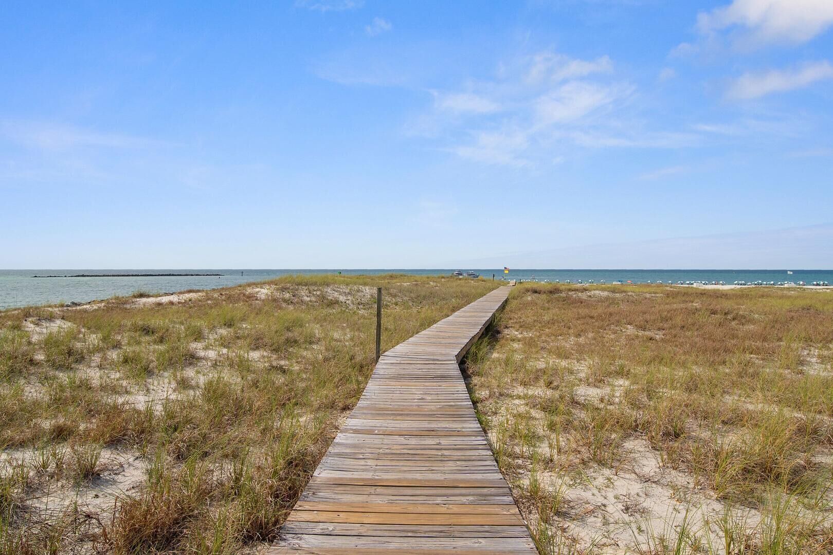 A wooden boardwalk leading to a beach with dunes and a clear sky.