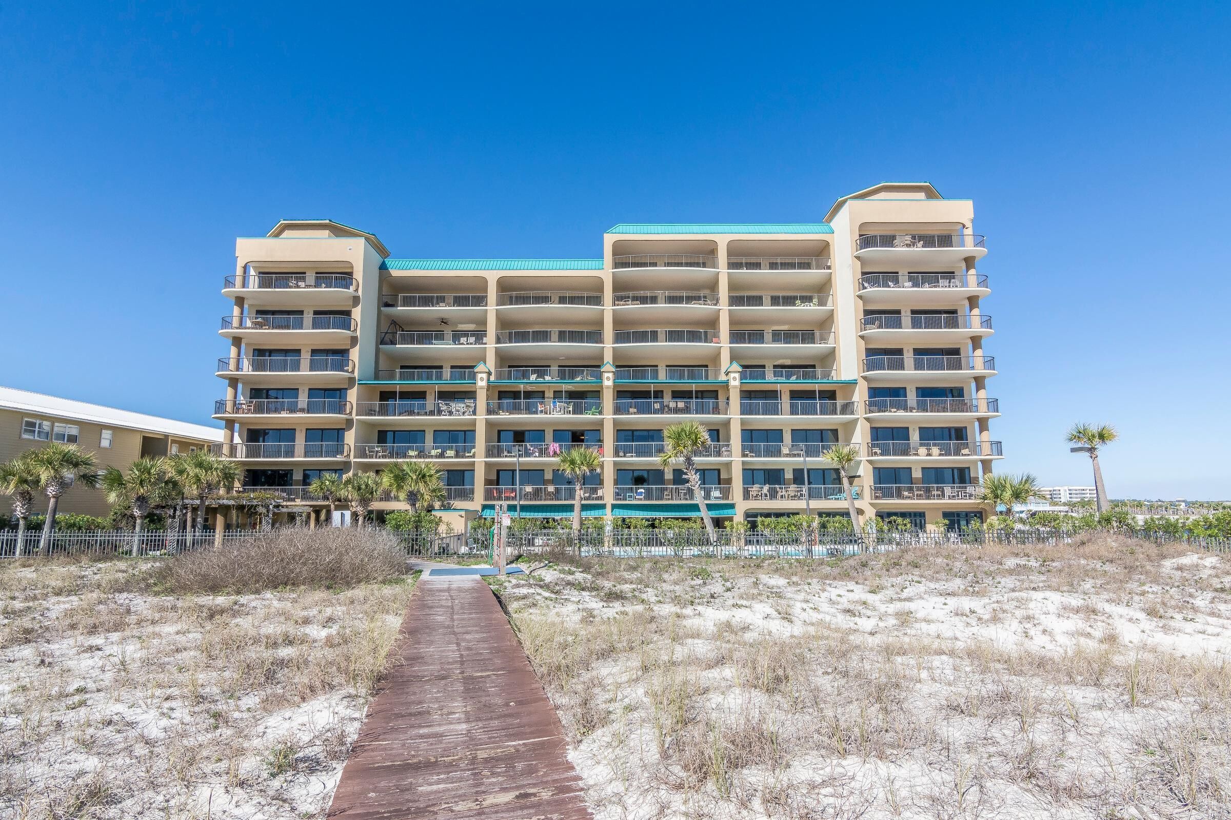 A multi-story hotel with balconies, a sandy beach in front, and a clear blue sky.