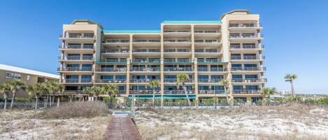 A multi-story hotel with balconies, a sandy beach in front, and a clear blue sky.