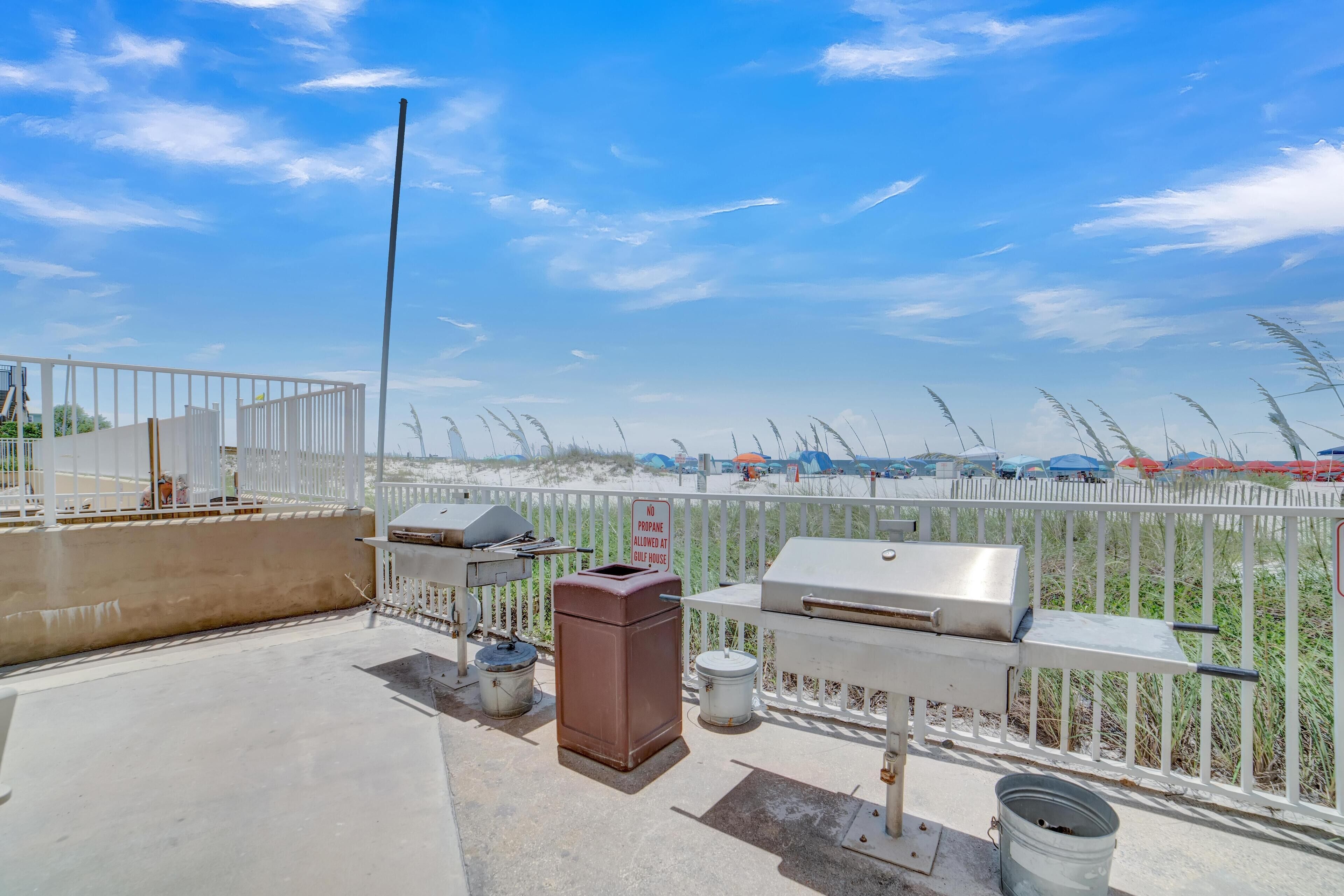 A rooftop patio with barbecue grills, a trash can, and a grill cover.