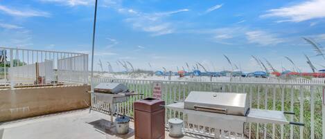 A rooftop patio with barbecue grills, a trash can, and a grill cover.