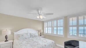 A bedroom with a bed, nightstands, a chair, and a ceiling fan. - Gulf House 401 (Gulf Shores)