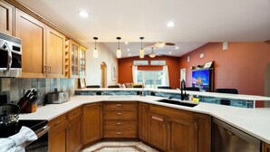 Una cocina con gabinetes de madera, estufa de acero inoxidable, horno empotrado, un lavamanos y un ventilador de techo.