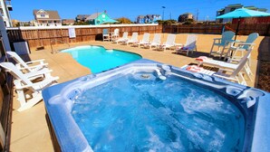 Um quintal com piscina e banheira de hidromassagem, cercado por cadeiras de descanso.
