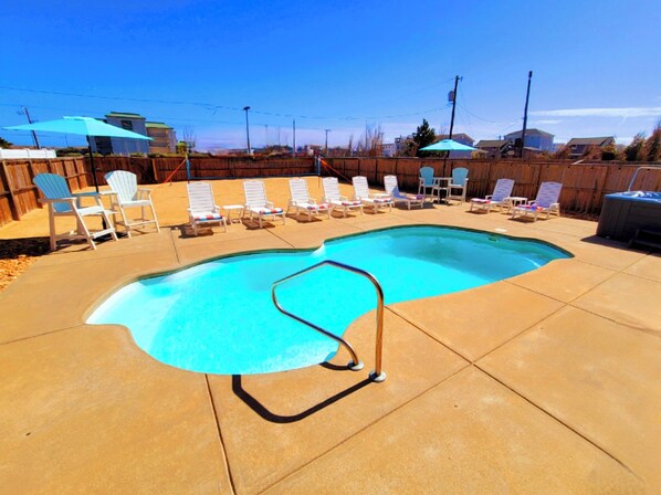 A backyard with a swimming pool, lounge chairs, and a wooden fence.