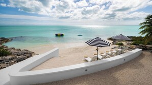A beach with white lounge chairs, striped umbrellas, and a clear view of the ocean. - Opaline Villa  4 BR 2Bath Ocean Front Villa (Providenciales)