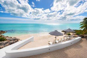 A beach with white lounge chairs and striped umbrellas, a clear sky, and turquoise water.