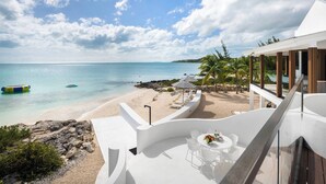A modern resort with a balcony overlooking a beach, lounge chairs, and a dining area with a table and chairs. - Opaline Villa  4 BR 2Bath Ocean Front Villa (Providenciales)