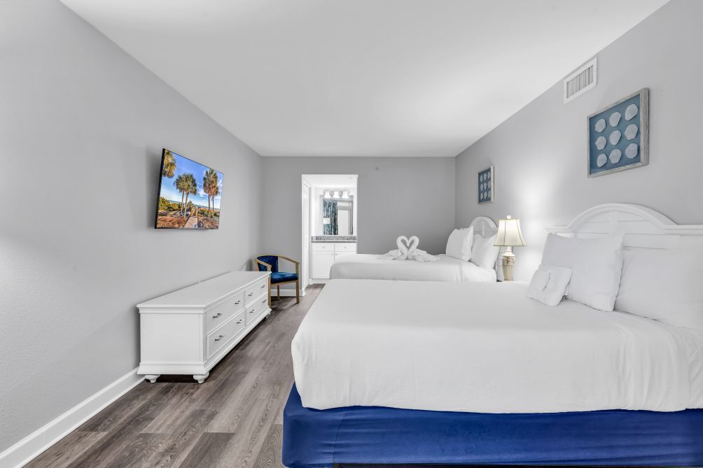 Une chambre avec un grand lit, une commode, une chaise et un tableau accroché au mur.