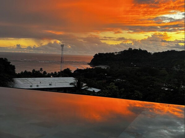 A coastal landscape with a sunset, a prominent communication tower, and a mix of residential buildings and greenery.