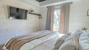 A bedroom with a bed, a ceiling fan, a mounted TV, and a window with curtains.