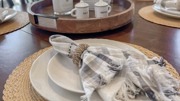 A dining table with a white vase, two salt and pepper shakers, a woven placemat, and a plaid cloth.