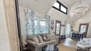 A spacious living room with a high ceiling, a dining area with a table and chairs, and a cozy seating area with a sofa and ottoman.