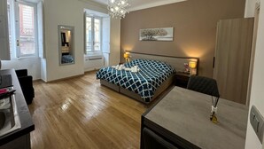 Un dormitorio con cama, mesitas de noche, escritorio, silla, candelabro y ventana.