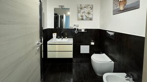 Un baño moderno con lavamanos blanco, azulejos negros, inodoro y bidé.