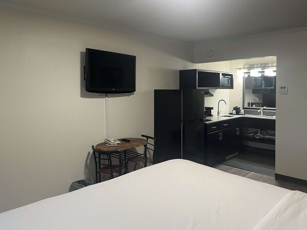 Ein Hotelzimmer mit Bett, kleinem Tisch mit Telefon und Fernbedienung, an der Wand montiertem Fernseher, Küchenzeile mit Mikrowelle, Spüle und Schränken.
