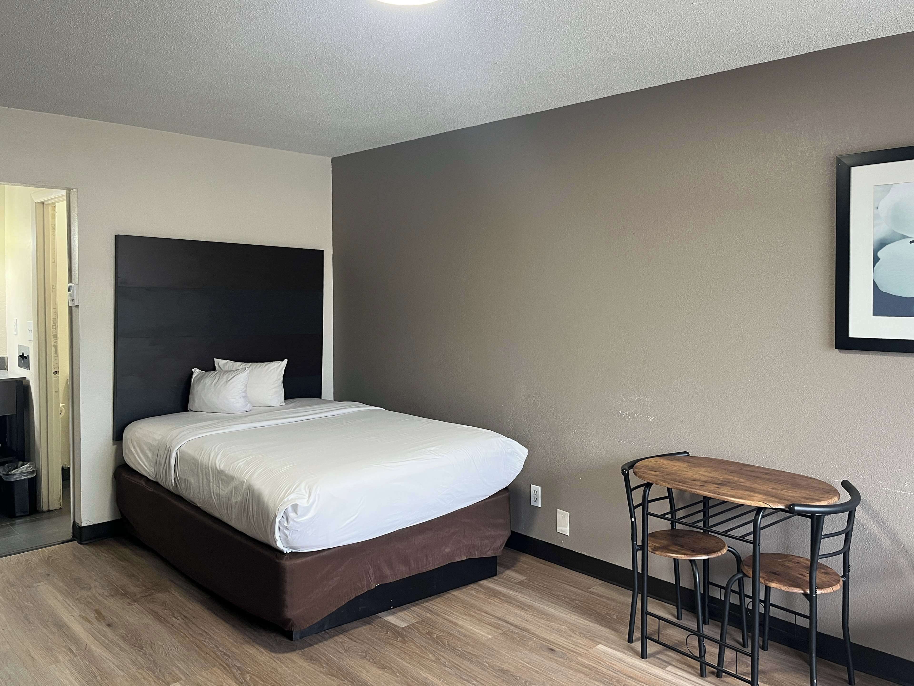 A hotel room with a bed, a small table with two chairs, and a framed picture on the wall.
