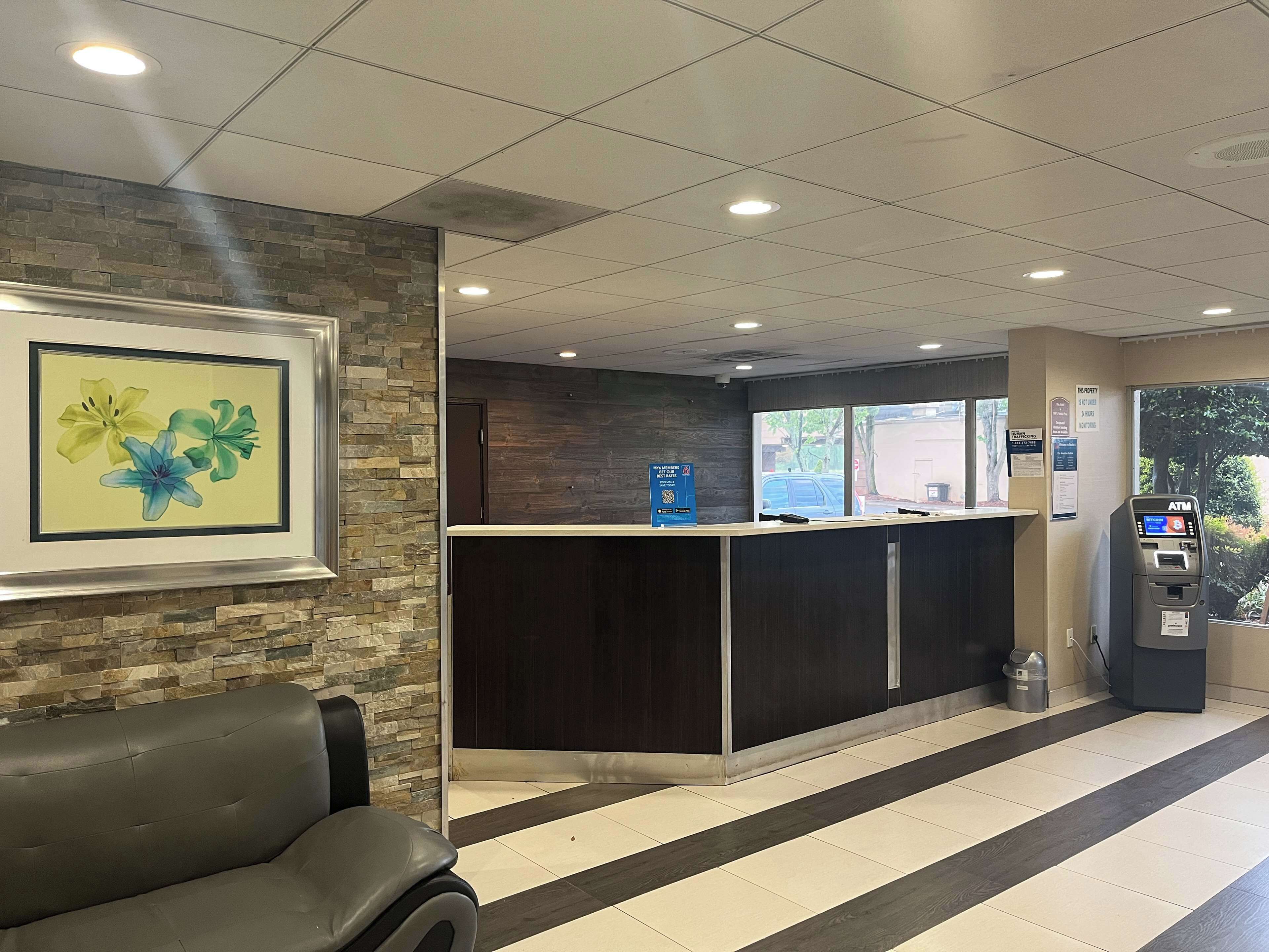 A reception area with a stone wall, a framed floral artwork, a reception desk, an ATM, and a trash bin.