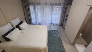 Een hotelkamer met een bed, kussens, een handdoek, een kamerkleed met dessin en dunne gordijnen.