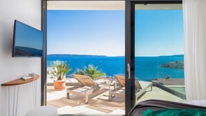 A balcony with a view of the sea, a TV mounted on the wall, and a small table with a plant.