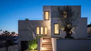 A modern two-story house with a staircase leading to the entrance, surrounded by a landscaped garden.