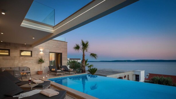 A modern outdoor pool area with lounge chairs and a view of the sea.