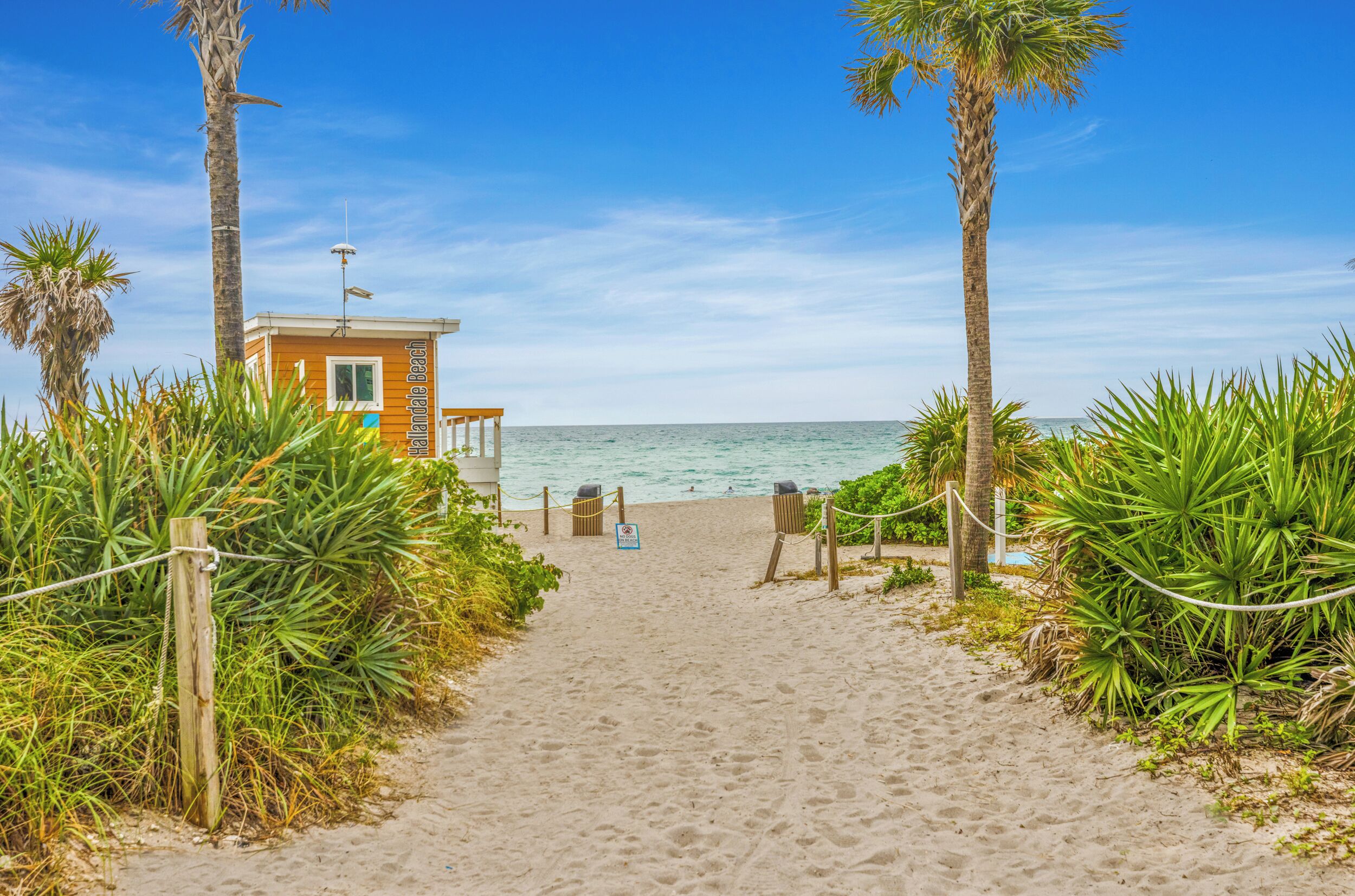 A sandy beach path leading to a lifeguard tower with a clear view of the ocean.