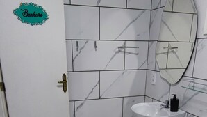 Ein Badezimmer mit weißen Marmorfliesen, einem Waschbecken, einer Toilette und einem Spiegel.