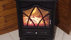 Ein schwarzer Kaminofen mit Glastür, aufgegestellt auf einem Fliesenboden vor einer Holzwand.
