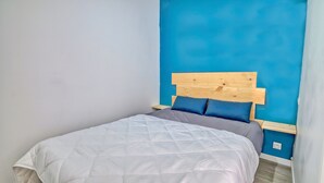 A single bed with a wooden headboard, a grey duvet, and two blue pillows. - Le Grain de Sable (Agde)