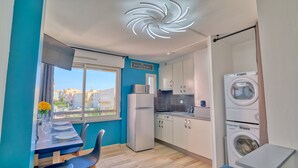 A modern kitchen with a view of the sea, a dining area with a table set for two, and a washing machine. - Le Grain de Sable (Agde)