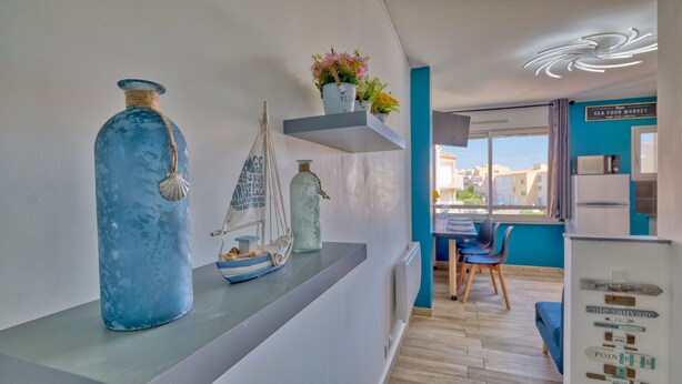 A modern kitchen with a view of the city, a dining area with a table and chairs, and decorative items on the counter. - Le Grain de Sable (Agde)