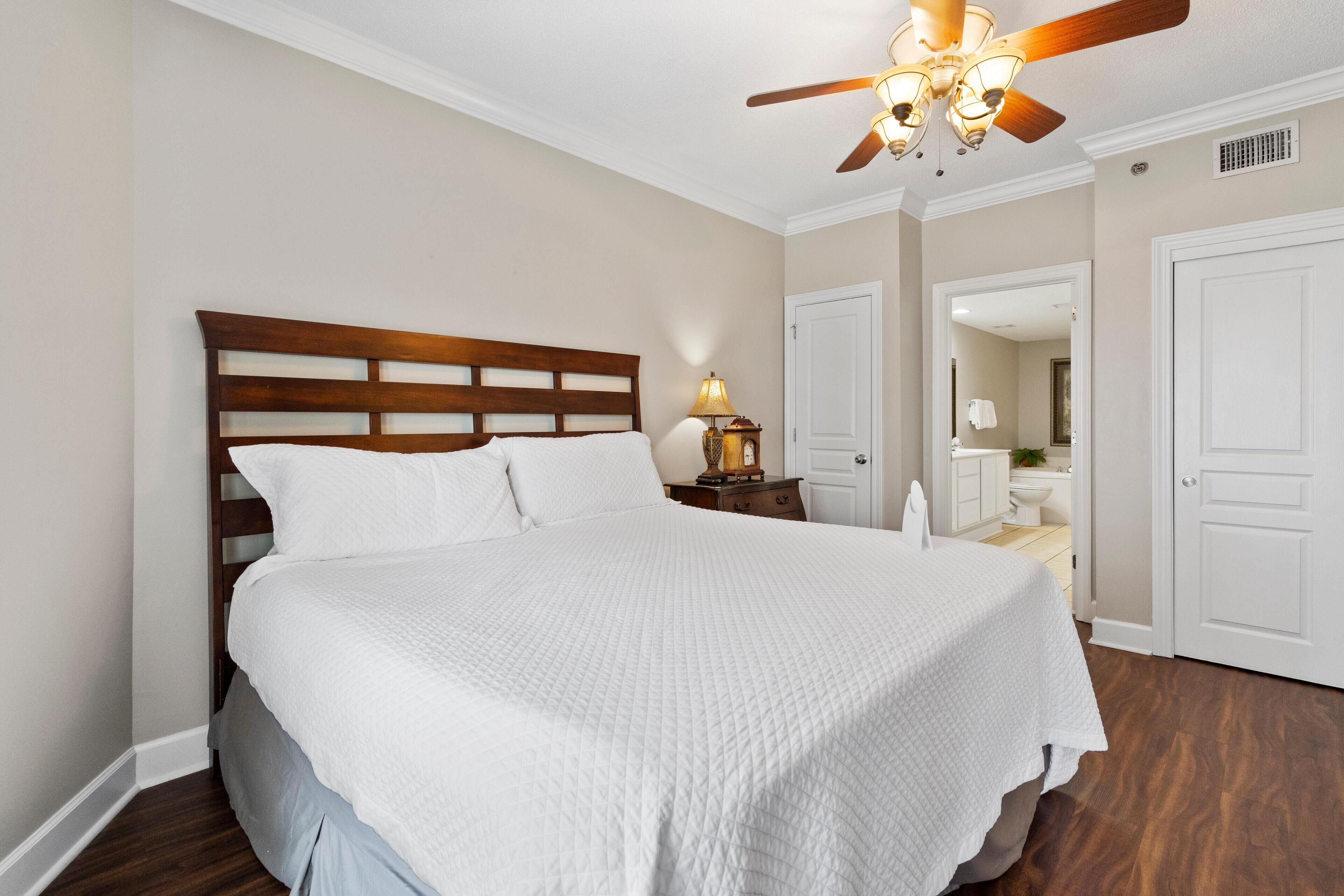 A neatly made bed in a bedroom with a wooden headboard, a ceiling fan, and a nightstand with a lamp.
