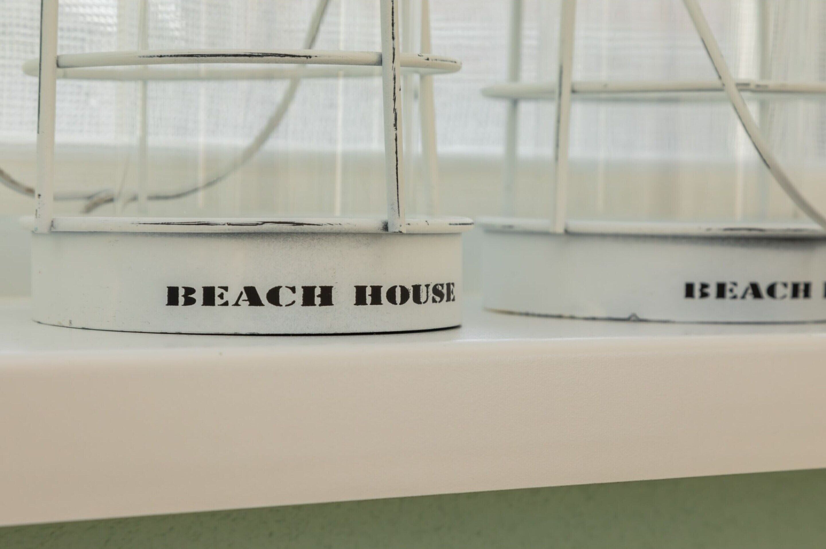 En närbild på en vit, väderbiten skylt med texten ”BEACH HOUSE”.