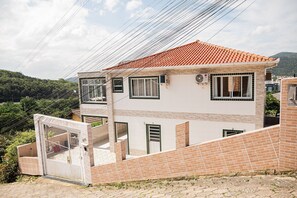 A two-story house with a red-tiled roof, a gated entrance, and a view of a mountainous landscape.