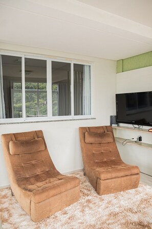 Ein Zimmer mit zwei braunen Lounge-Sesseln, einem Fernseher auf einem Schrank und einem Fenster mit Vorhängen.