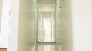 A long, narrow hallway with white walls and a glossy floor, leading to a door at the end. - Morada Monte Verde - Florianópolis-SC (Florianópolis)