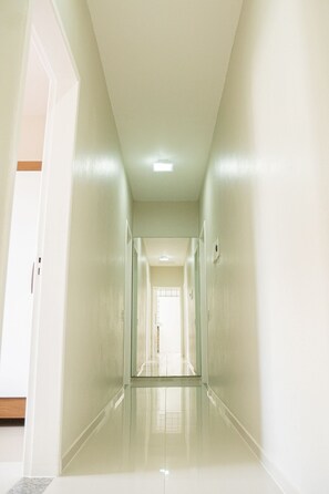 A long, narrow hallway with white walls and a glossy floor, leading to a door at the end. - Morada Monte Verde - Florianópolis-SC (Florianópolis)