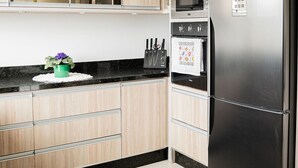 A modern kitchen with wooden cabinets, a stainless steel refrigerator, a microwave, and a sink. - Morada Monte Verde - Florianópolis-SC (Florianópolis)