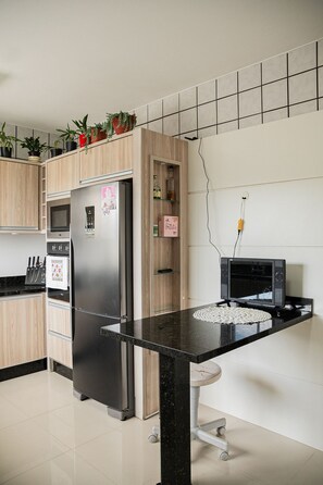 A modern kitchen with a stainless steel refrigerator, wooden cabinets, a microwave, and a small black TV on a stand. - Morada Monte Verde - Florianópolis-SC (Florianópolis)
