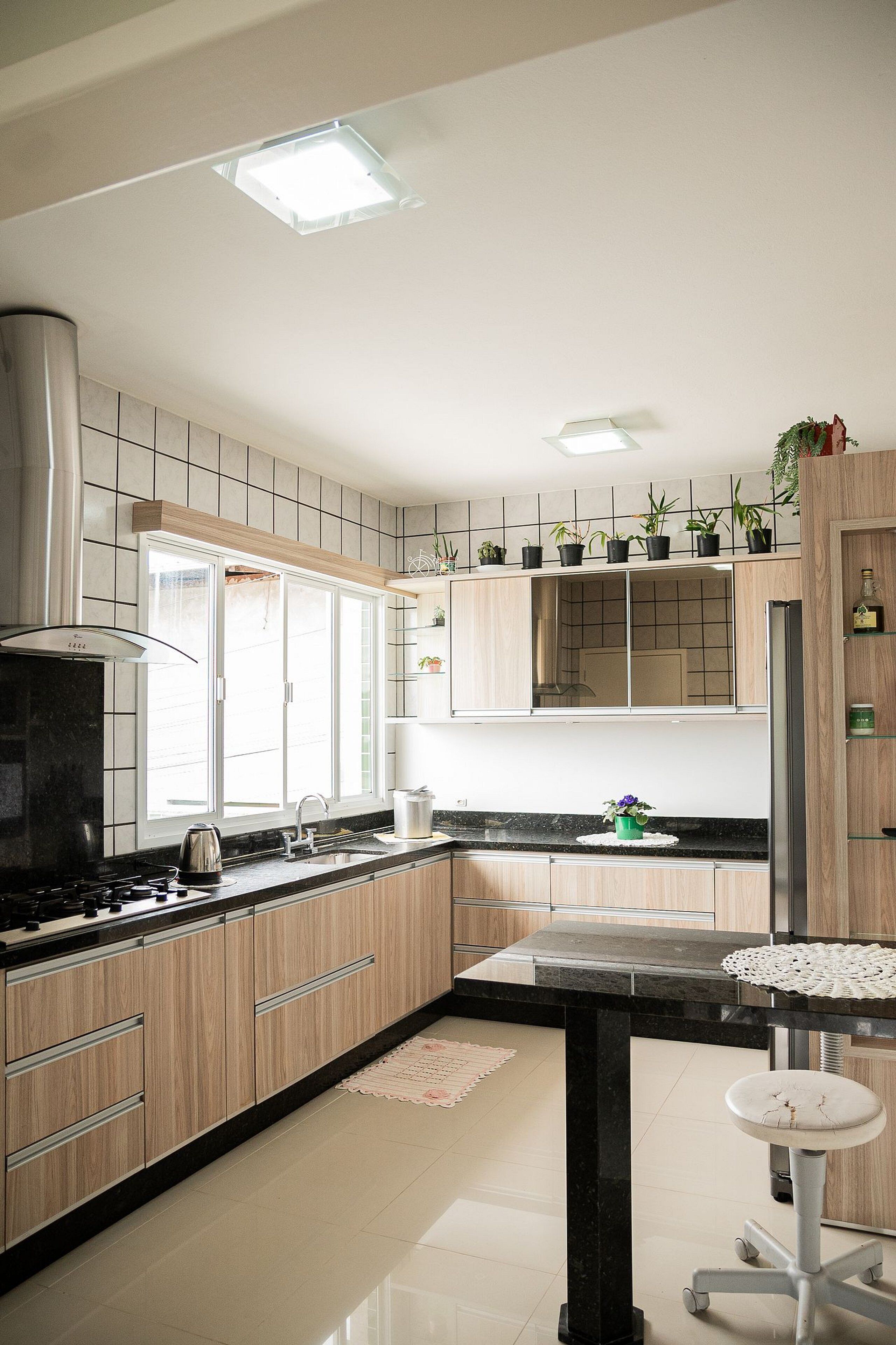 A modern kitchen with a black countertop, wooden cabinets, a stainless steel range hood, and a window with a view.
