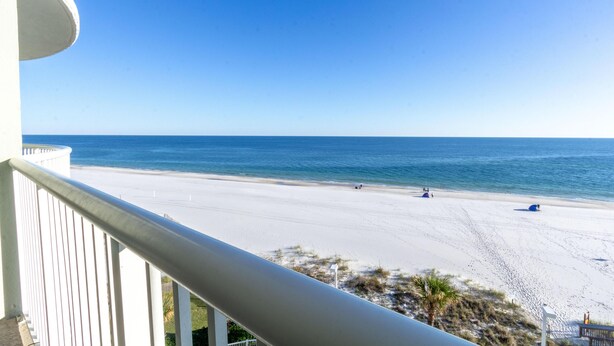 A beach view from a balcony with a railing, clear sky, and calm sea. - Tradewinds 503 (Orange Beach)