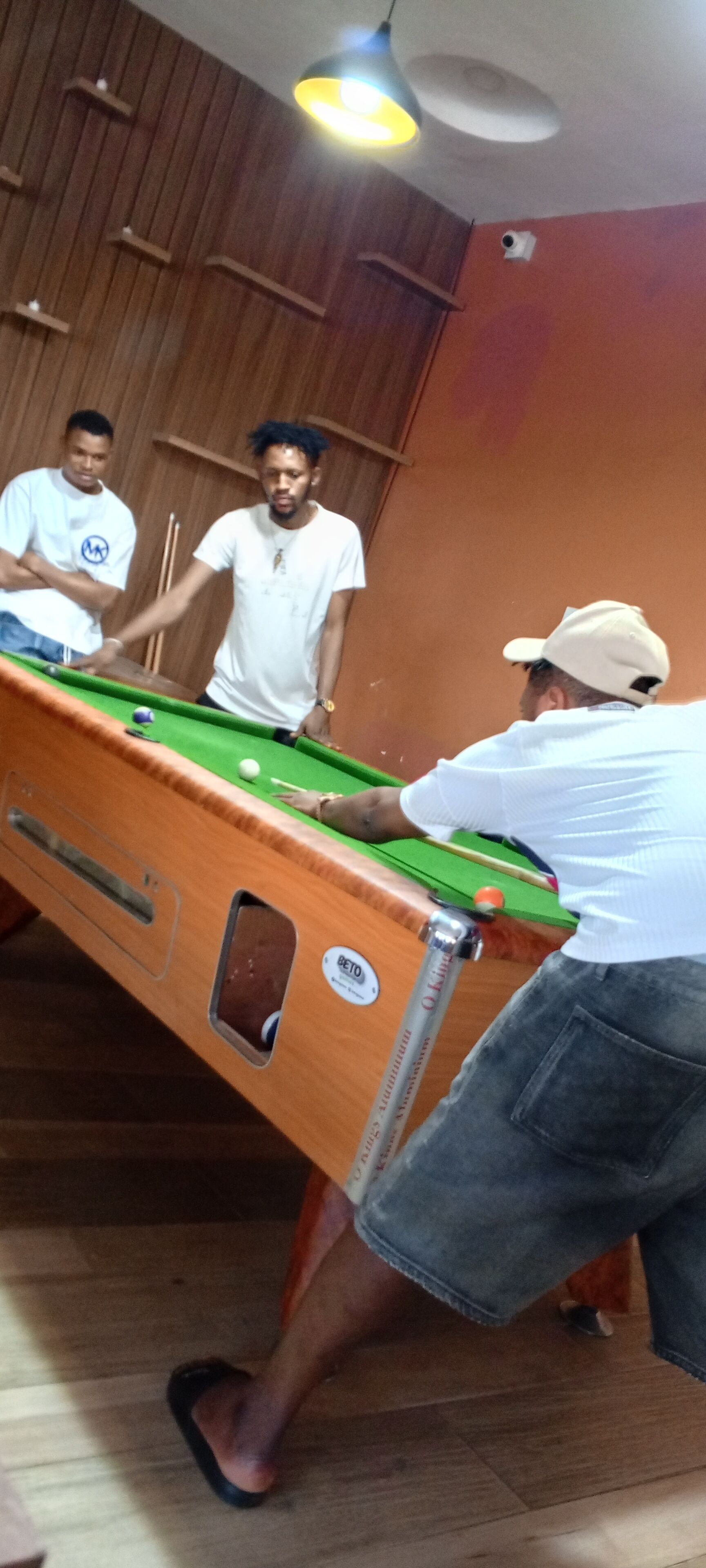 A pool table in a room with wooden paneling and a ceiling light.