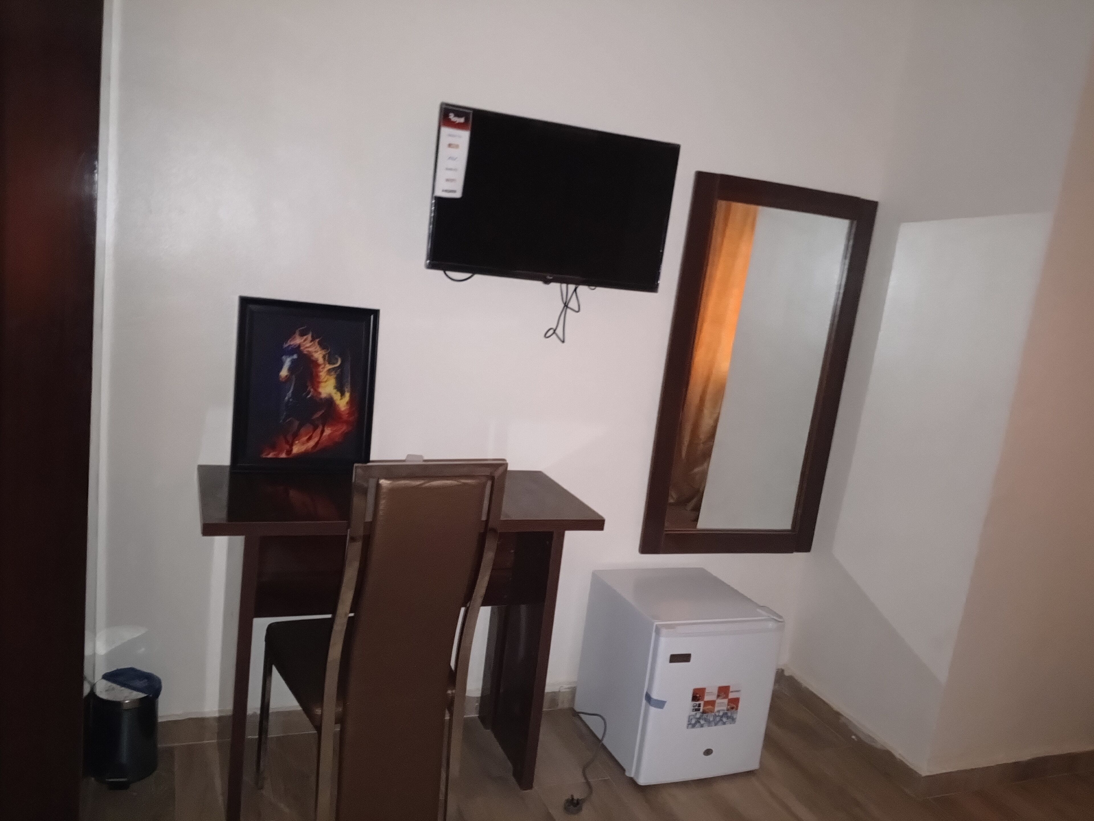 Ein kleines Zimmer mit Schreibtisch, Stuhl, Fernseher und Kühlschrank.
