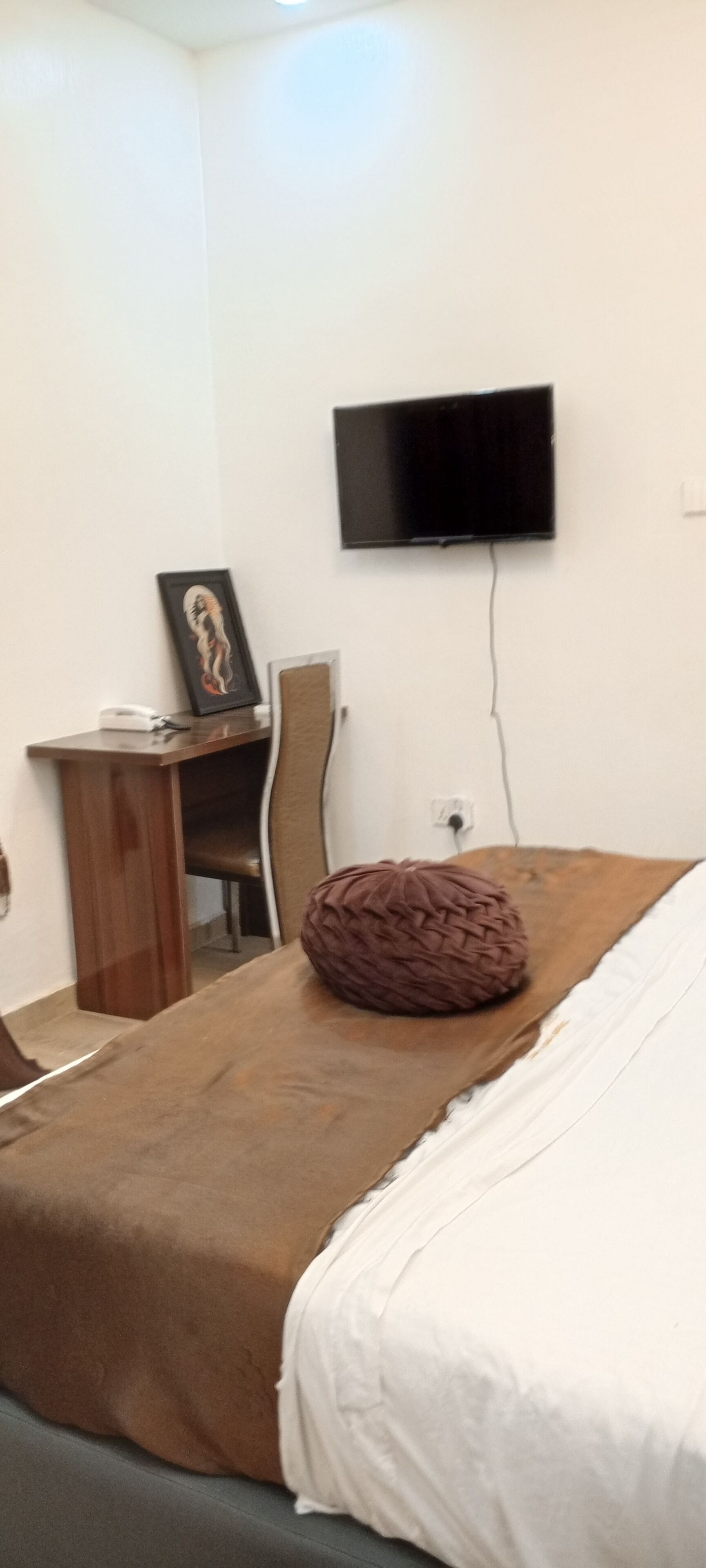 A bedroom with a bed, a desk, a chair, and a flat-screen TV mounted on the wall.