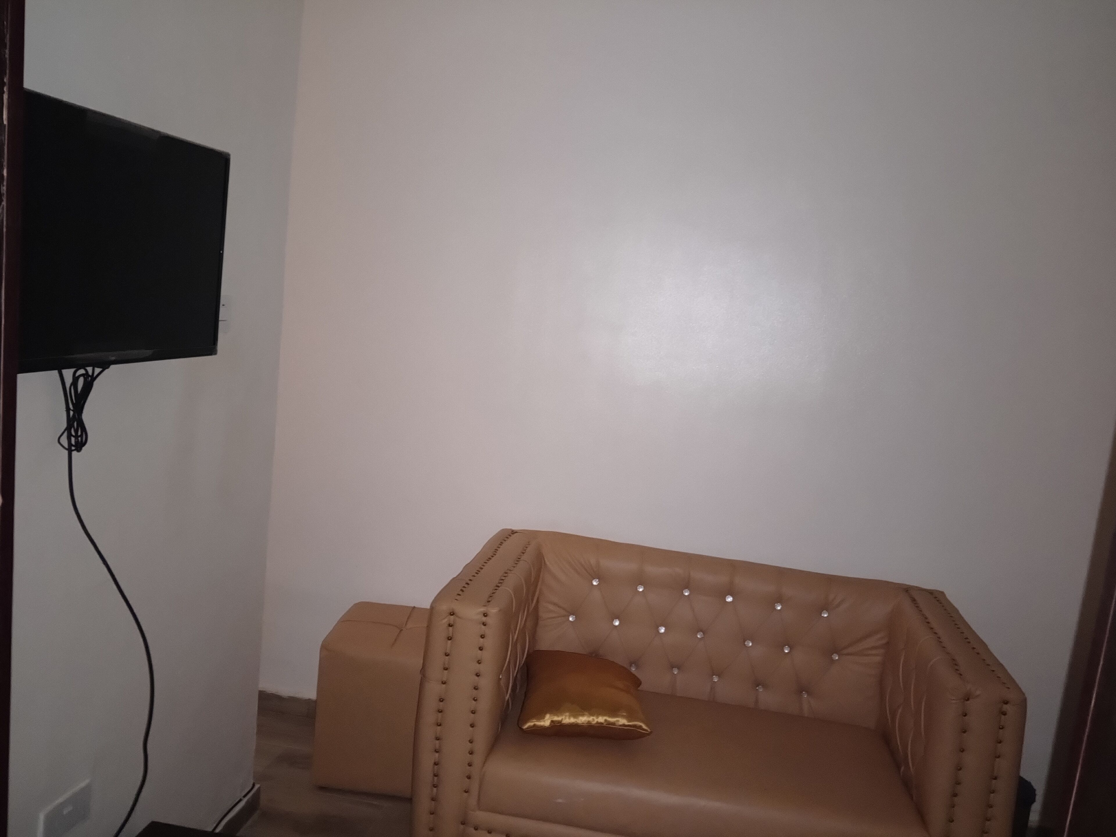 A room with a brown leather sofa, a television mounted on the wall, and a power outlet on the floor.